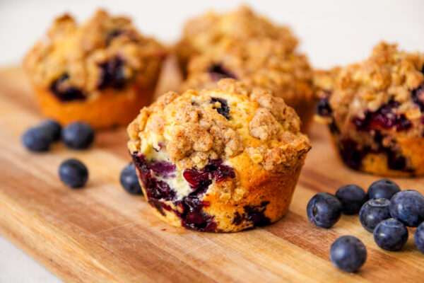 Freshly baked blueberry muffins with an oat crumble topping on a natural wooden board.