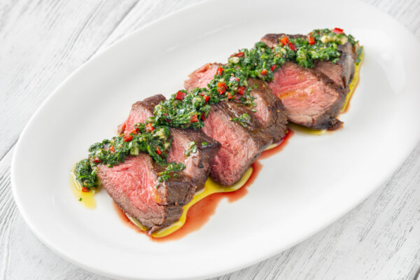 Portion of sliced strip steak with Chimichurri sauce