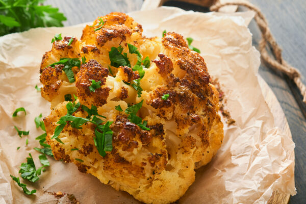 Whole baked cauliflower with spices and herbs served on a wooden rustic board.