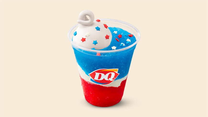 A Dairy Queen frozen drink layered in red, white, and blue with whipped topping decorated with red and blue star sprinkles, presented against a plain beige background.