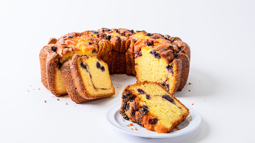Blueberry Bundt cake with several slices cut and displayed on a white plate, showing a moist yellow interior with blueberries throughout.
