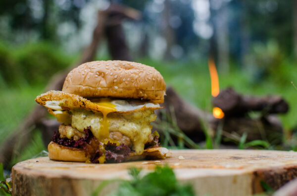 home made chicken burger with curry mayo sauce and lettuce, tomato, egg, green and yellow paprica as compliment. bushcraft cooking style with campfire.