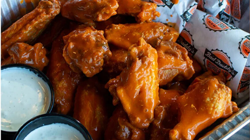 Basket of buffalo chicken wings coated in orange sauce, served with two cups of ranch dressing for dipping.