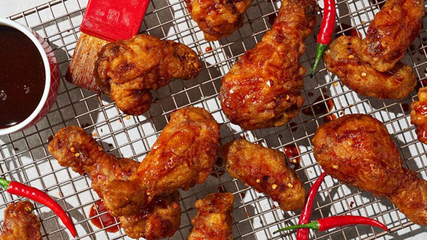 Barbecue-glazed fried chicken wings and drumsticks arranged on a wire rack with a bowl of barbecue sauce, a basting brush, and red chili peppers.