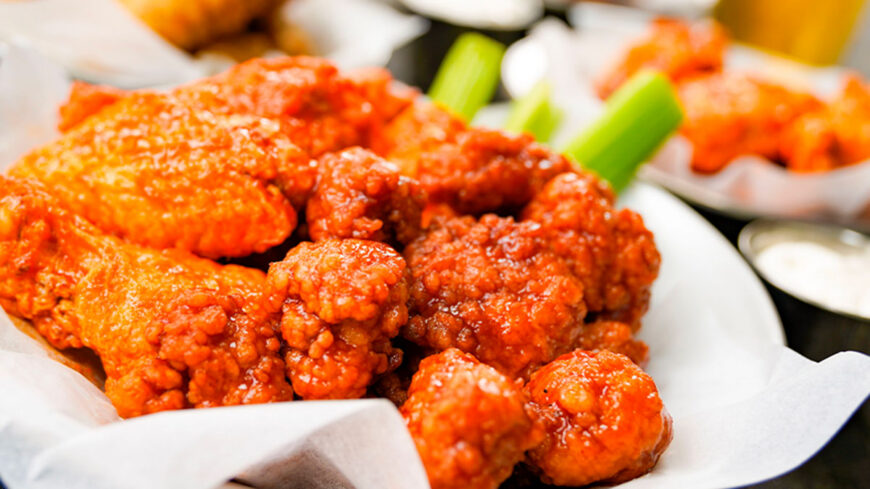 Basket of crispy Buffalo chicken wings coated in spicy orange-red sauce, served with celery sticks and ranch dressing.