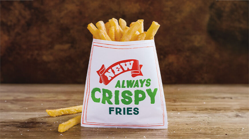 Paper carton filled with golden French fries on a wooden table, labeled "New Always Crispy Fries."