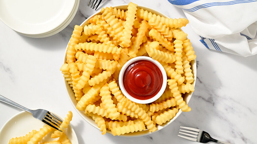 Bowl of crinkle-cut French fries surrounding a small bowl of ketchup, viewed from above.