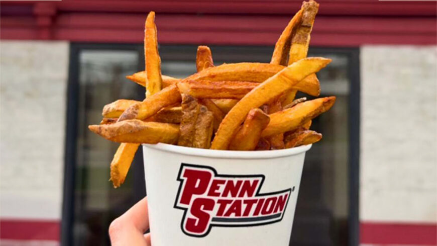 Cup of thick-cut fries held outdoors in front of a Penn Station restaurant.