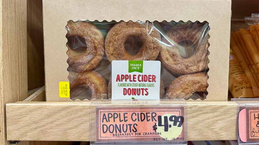 Box of Trader Joe’s apple cider donuts dusted with cinnamon sugar, displayed on a store shelf.