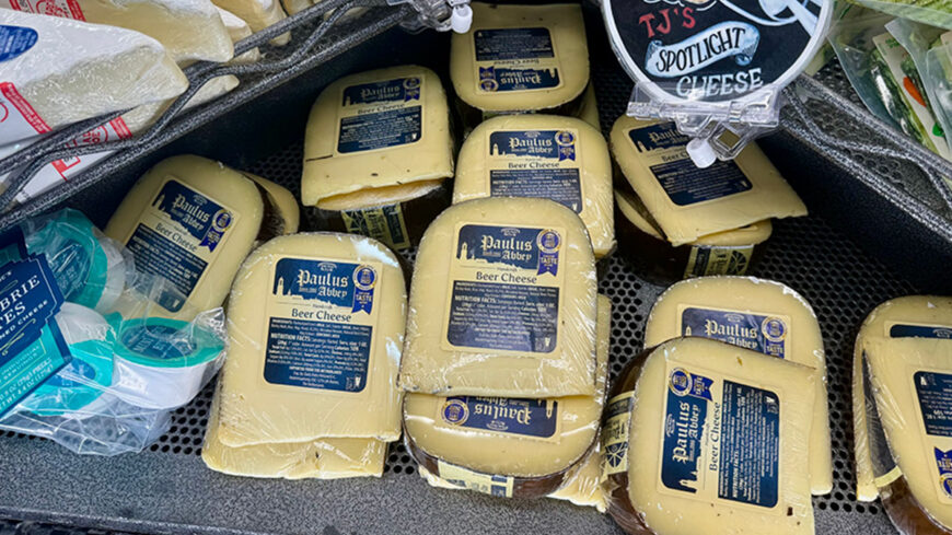 Packages of Trader Joe’s Paulus Beer Cheese arranged in a refrigerated display case.