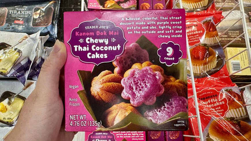 Trader Joe’s Kanom Dok Mai Chewy Thai Coconut Cakes in a purple box, showing colorful purple and golden flower-shaped coconut cakes; the package contains nine vegan cakes.
