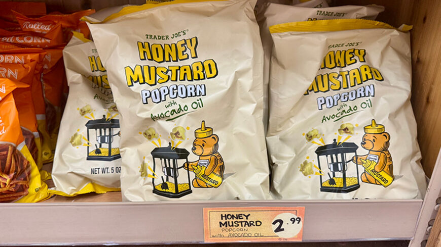 Bags of Trader Joe's Honey Mustard Popcorn made with avocado oil displayed on a store shelf, priced at $2.99.