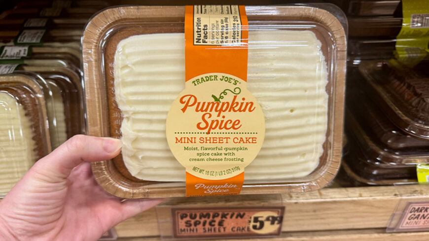 A hand holds a package of Trader Joe’s Pumpkin Spice Mini Sheet Cake, topped with cream cheese frosting.