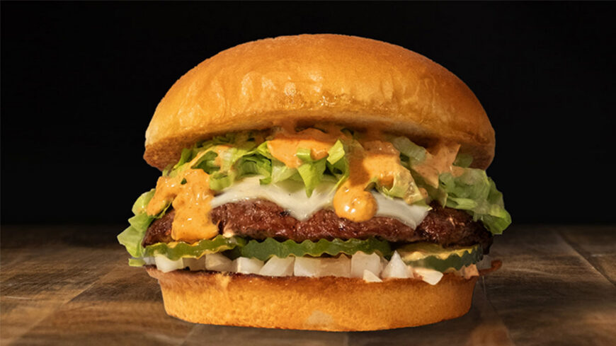 Cheeseburger with a toasted brioche bun, beef patty, melted white cheese, shredded lettuce, pickles, diced onions, and orange sauce.