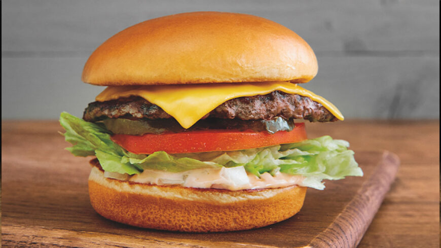 Cheeseburger on a toasted bun with a beef patty, melted yellow cheese, lettuce, tomato, pickles, onions, and creamy sauce.