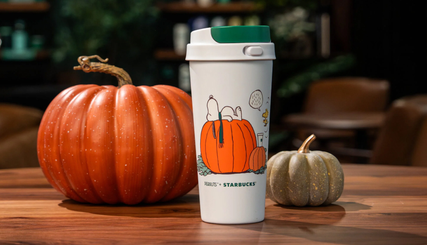 White tumbler with green top with picture of Snoopy laying on a pumpkin