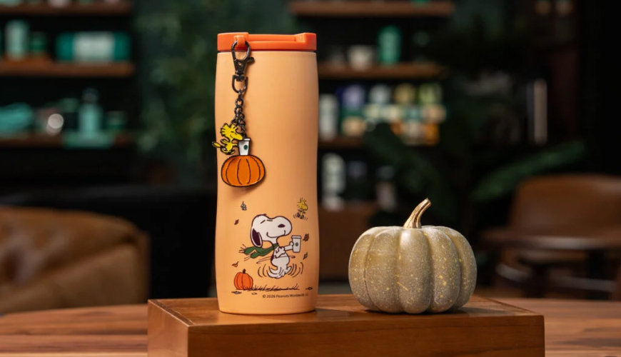 Orange tumbler with Woodstock and pumpkin key chain clipped to it and Snoopy on the cup