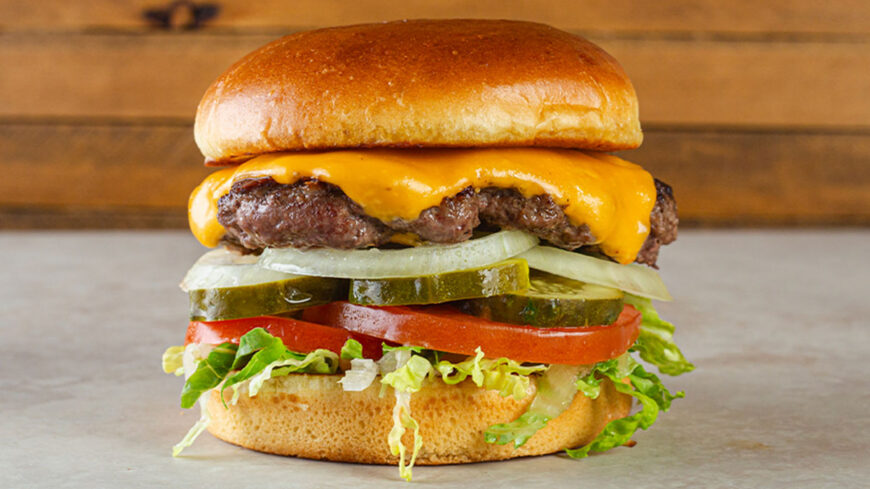 Cheeseburger with melted American cheese, lettuce, tomato, pickles, and sliced onions on a toasted bun.