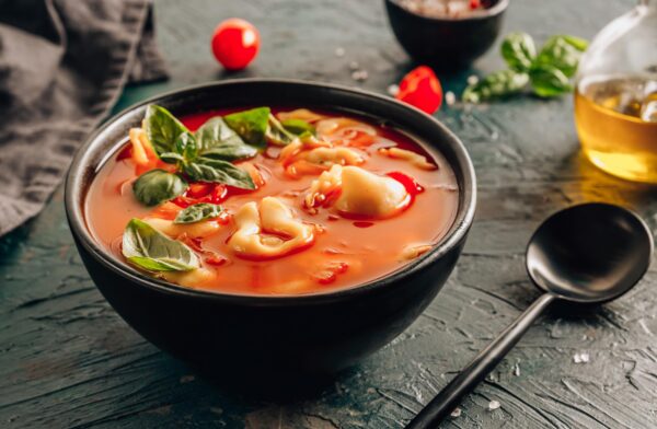 Tomato soup with tortellini in black bowl on dark background. Selective focus.