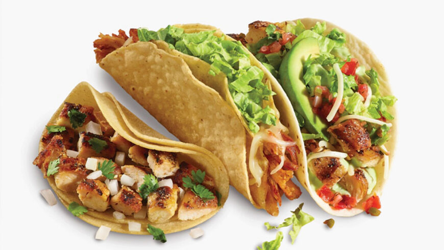 Three chicken tacos in soft and crispy tortillas, topped with lettuce, avocado, tomatoes, cheese, and grilled chicken.