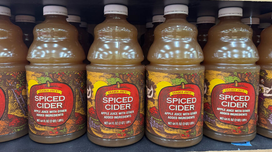 Row of Trader Joe’s Spiced Cider bottles on a store shelf, labeled as apple juice with added spices.
