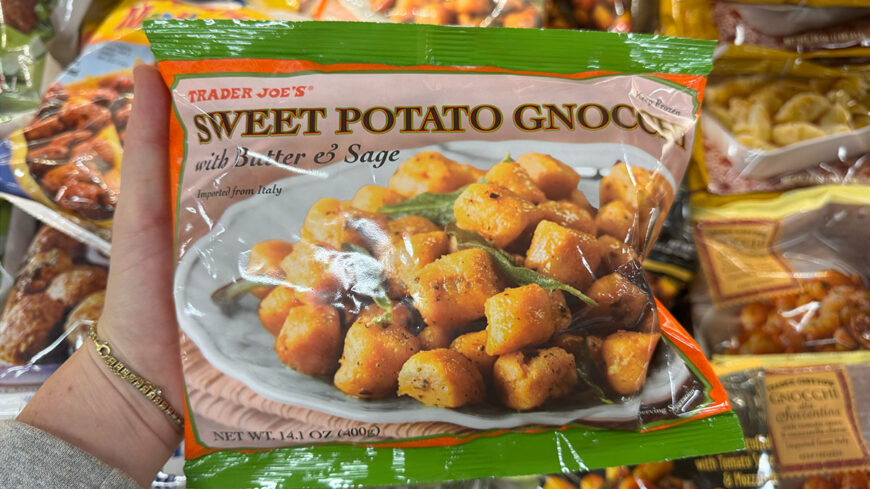 Hand holding a package of Trader Joe’s Sweet Potato Gnocchi with Butter & Sage in a frozen food aisle.