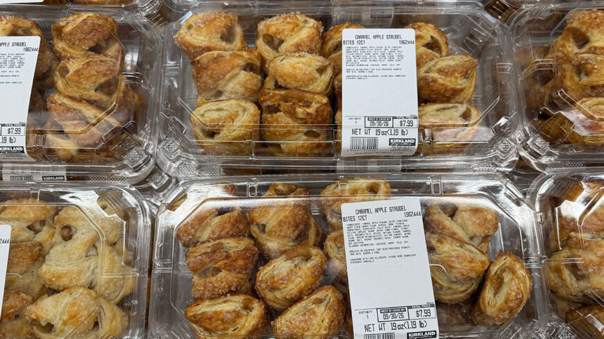Costco display of Kirkland Signature caramel apple strudel bites in clear plastic containers, with multiple golden-brown pastries visible and packages labeled $7.99.