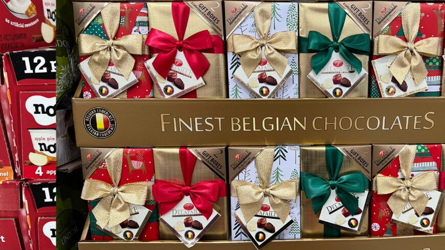 Display of decorated gift boxes filled with assorted Belgian chocolates, featuring large gold, red, green, and Christmas-themed bows.
