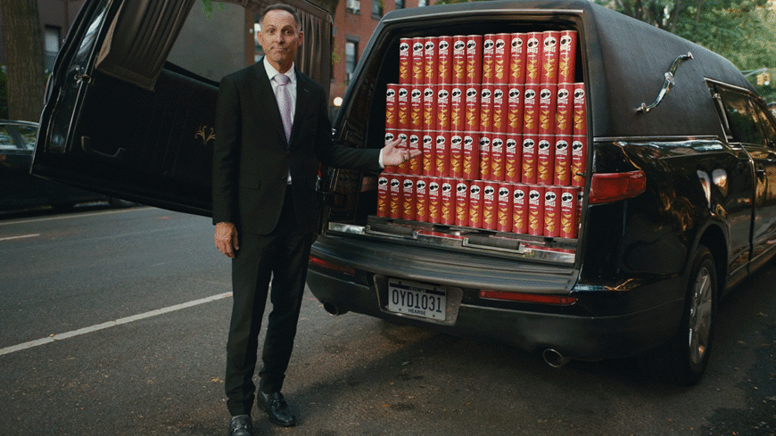 Funeral director standing next to hearse of pringles cans
