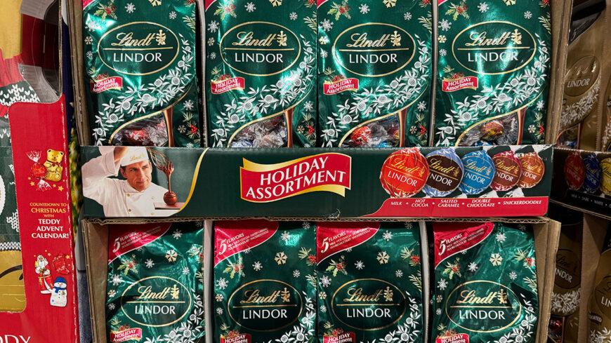 Display of green Lindt Lindor Holiday Assortment bags filled with assorted chocolate truffles.