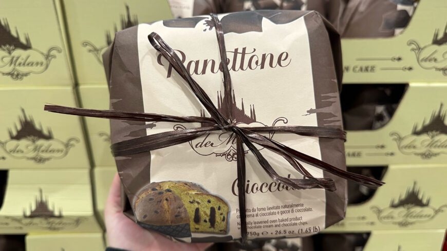 A wrapped 750-gram Italian panettone labeled “Panettone,” with chocolate cream and chocolate chips, held in front of stacked matching boxes.
