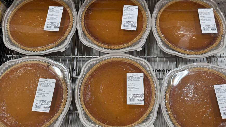 Packaged pumpkin pies in clear plastic containers displayed on a store shelf.